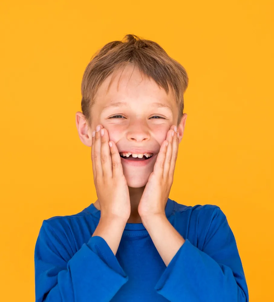 Smiling boy in a blue top, hands on his cheeks, orange background