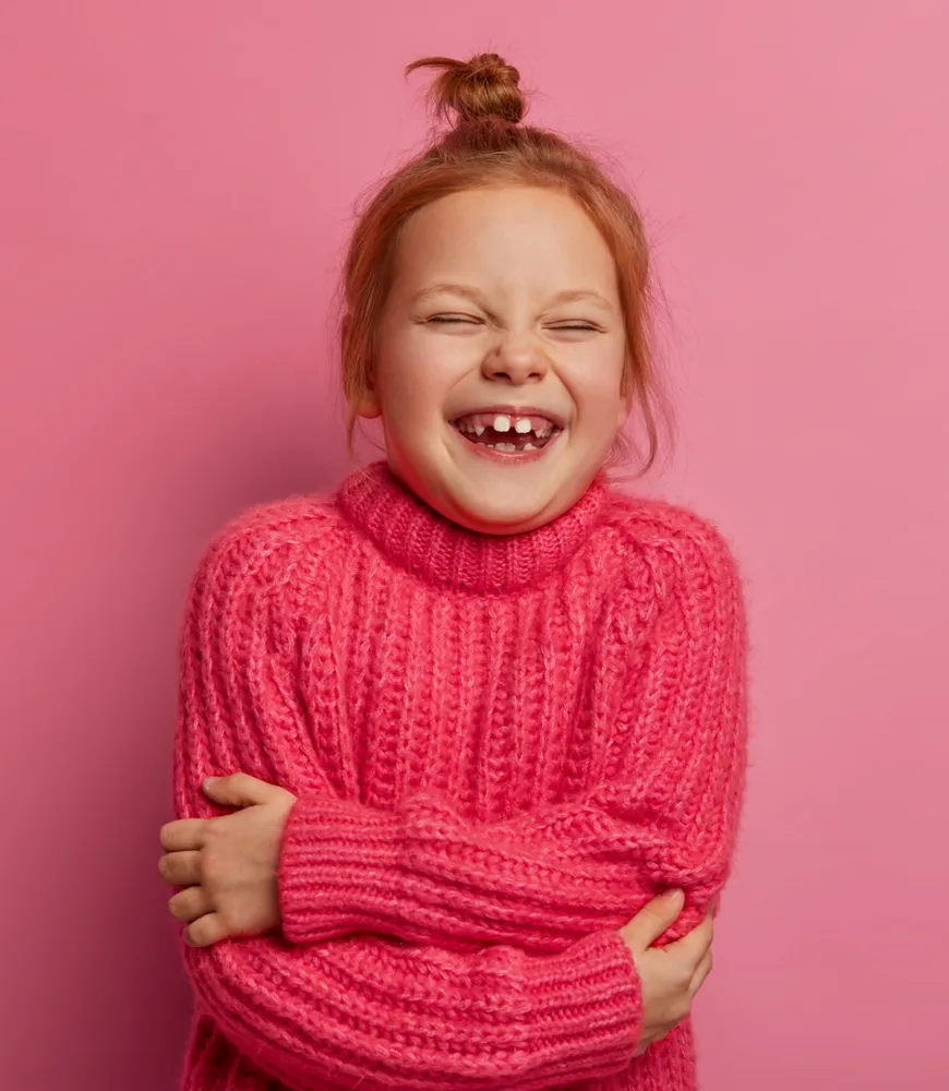 A girl in a pink knitted jumper laughing with her eyes closed